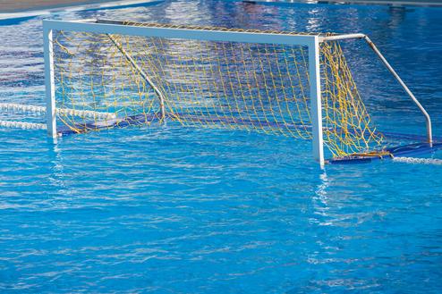 Wasserballtor mit gelbem Netz in einem blauen Schwimmbecken, teilweise im Wasser stehend.